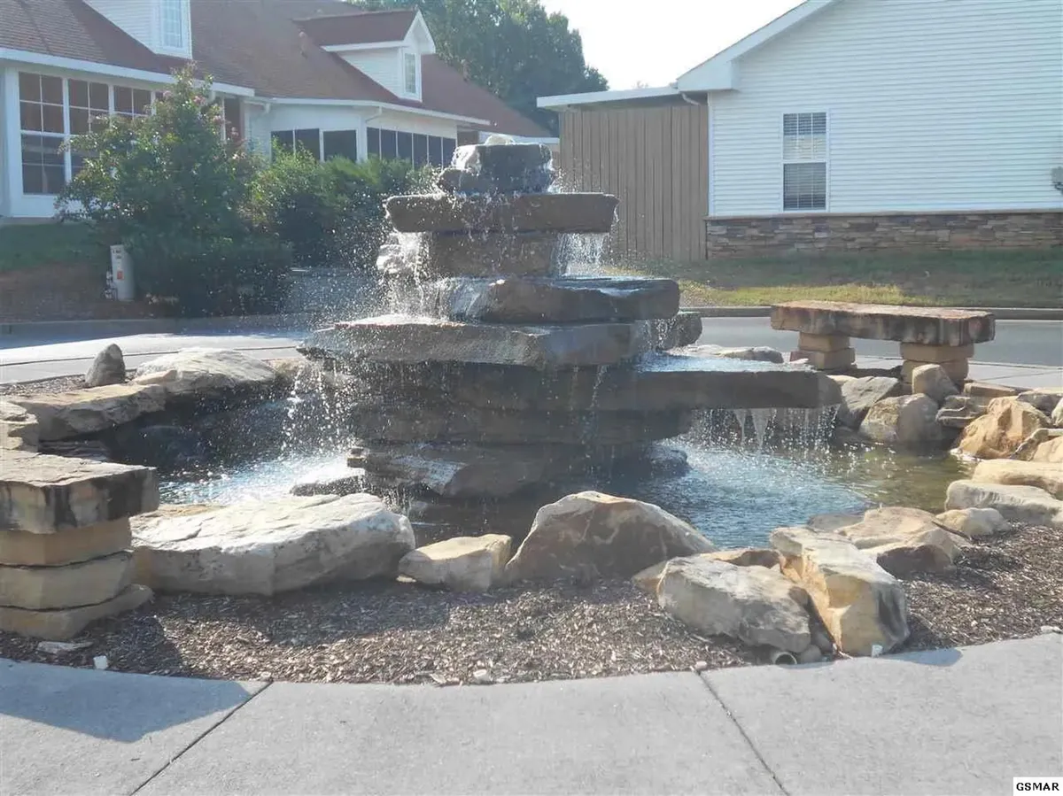 A tranquil exterior space with a water fountain surrounded by rocks and benches, designed for relaxing outdoors, enjoying nature, or sharing quiet moments together.