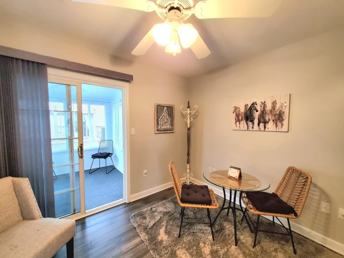 A relaxed dining area with stylish chairs and a table positioned near a glass door leading to a bright sunroom. Artwork of horses on the wall adds local charm, and the space is bathed in natural light, perfect for casual dining or social gatherings.