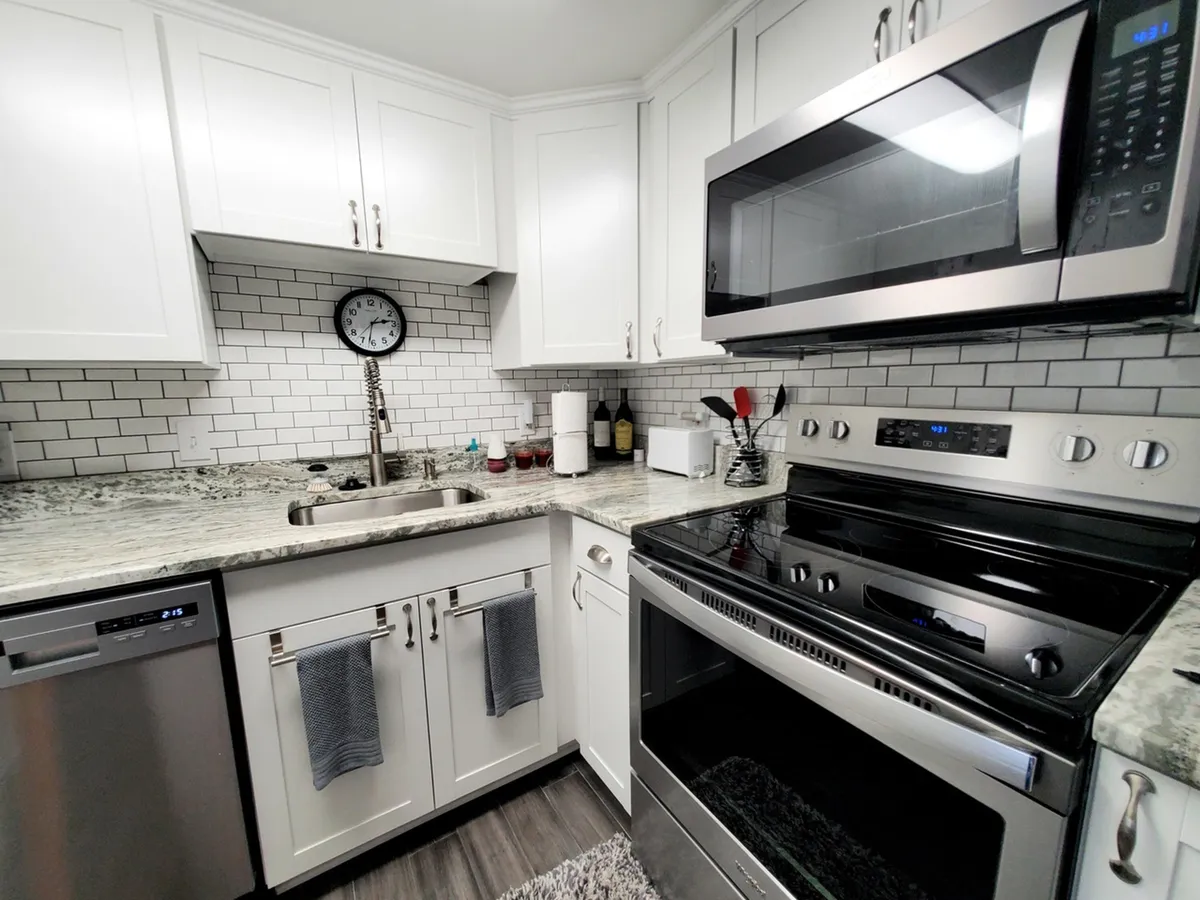 A cozy kitchen scene with granite countertops, stainless steel appliances, white cabinetry, a subway tile backsplash, and a wall clock. The space is designed for both cooking and socializing, evoking a warm, inviting mood.