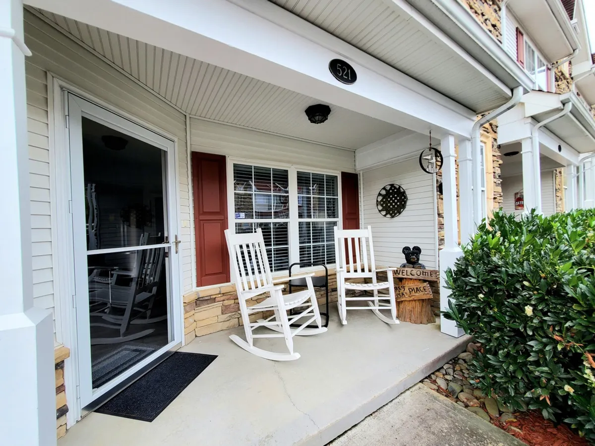 A welcoming exterior shot featuring classic rocking chairs on a front porch, a prominent welcome sign, and the inviting front door. The soft lighting and relaxed arrangement of chairs suggest a space perfect for unwinding after a day of group adventures.