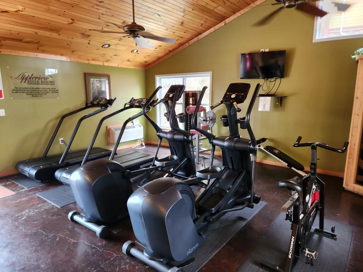 A spacious, well-lit fitness center equipped with elliptical machines, a treadmill, a stationary bike, and a television. The modern equipment is arranged to encourage both individual workouts and group fitness classes, reflecting a motivational and health-focused environment.