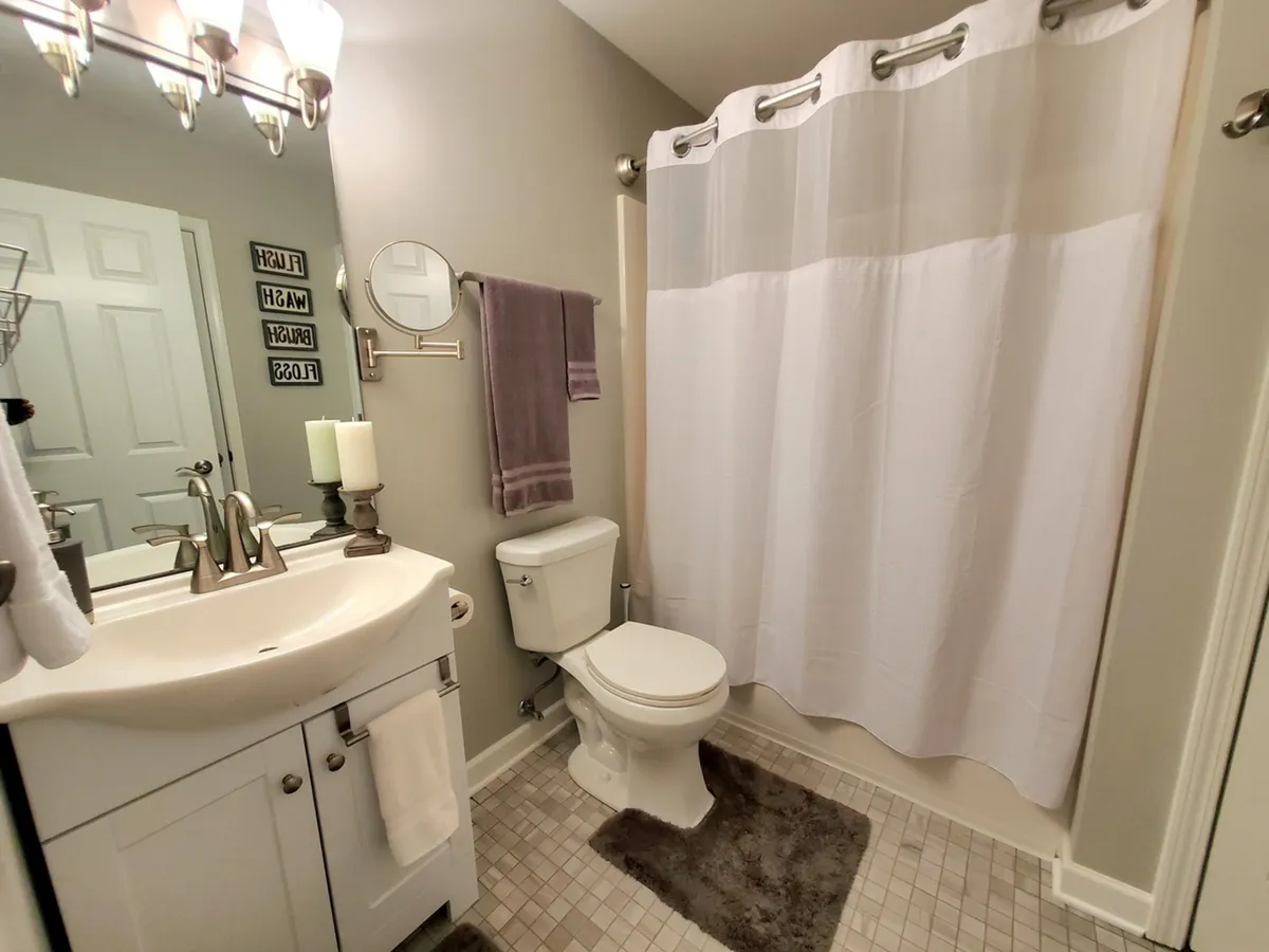 A bright, fresh bathroom with a vanity sink, mirror, shower curtain, toilet, and towel rack. The space feels clean, calm, and thoughtfully appointed for both morning routines and evening relaxation.