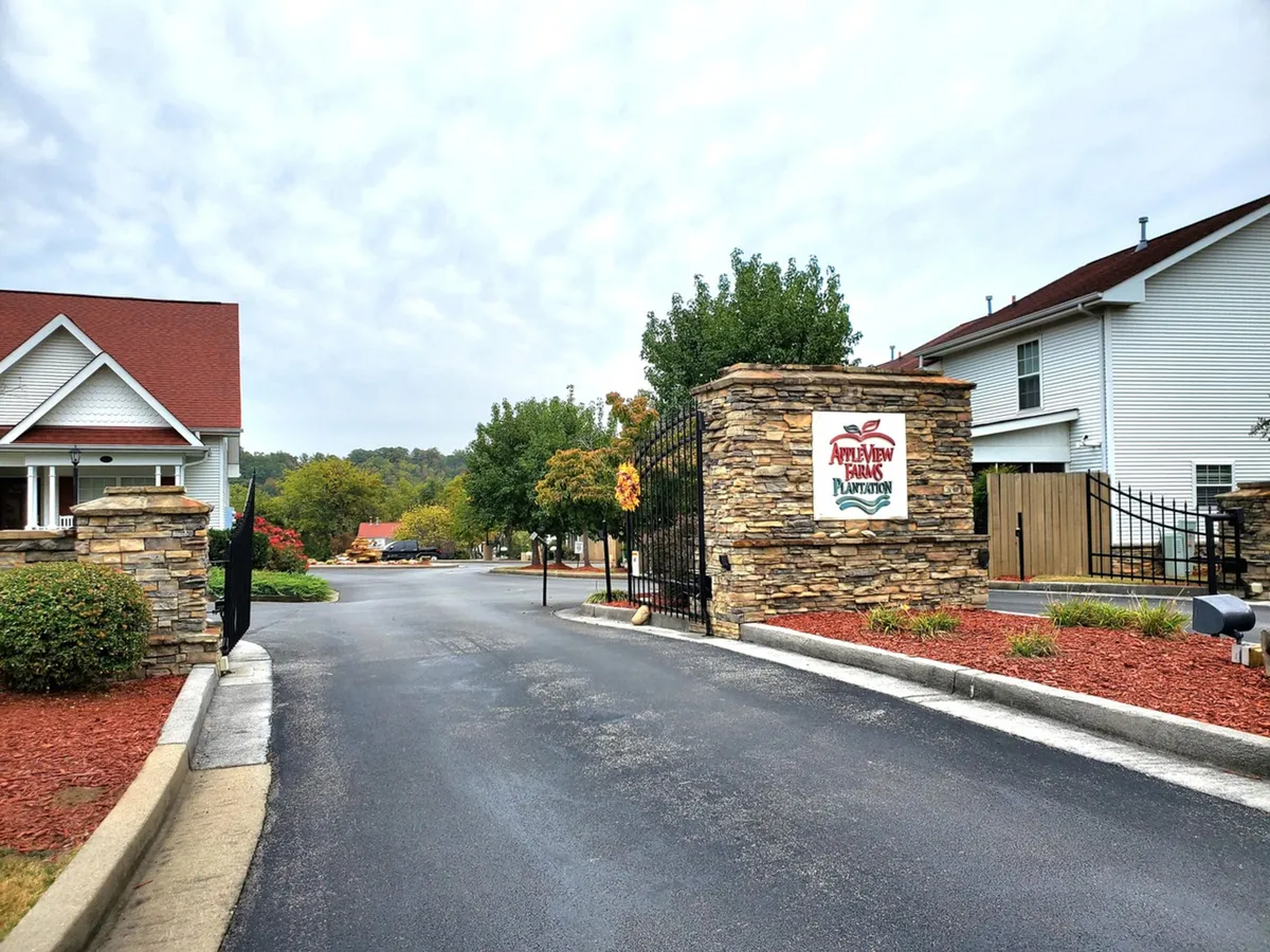 The beautifully landscaped stone entrance gate of the resort, with a decorative sign, lush greenery, and a paved road leading into the property, evoking a sense of arrival and welcome.